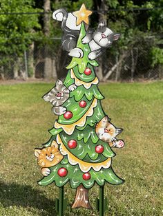 a wooden christmas tree with cats on it in the grass next to a chain link fence