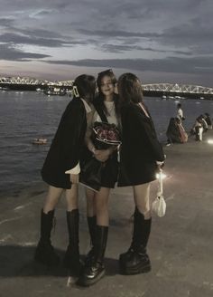 three young women standing next to each other near the water at night with lights on