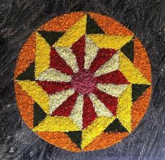 a circular design made out of flowers on top of a black stone floor with red, yellow and orange petals