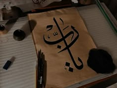 an arabic calligraphy is displayed on a table with other art supplies and items around it