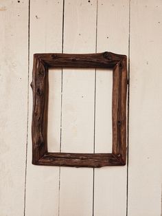 an old wooden frame hanging on a white painted wood wall with a plant in the corner