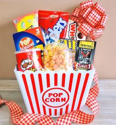 a popcorn box filled with snacks and candy on top of a wooden table next to a red ribbon