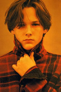 a young man wearing a red and black plaid shirt with his hand on his neck