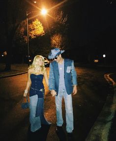 two people standing next to each other in the street at night with one person wearing a cowboy hat