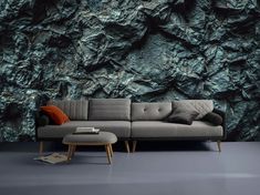 a couch sitting in front of a wall covered in green and black rock formation paper