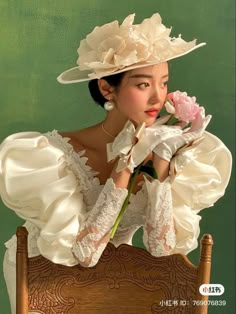 a woman in a white dress and hat holding a pink flower with her right hand