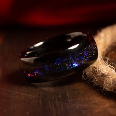 a black ring with blue and red speckles sitting on top of a wooden table