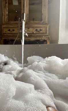 a bathtub filled with foam and water coming out of the faucet next to a dresser