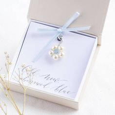 a white box with a blue ribbon around it and a flower charm hanging from the front