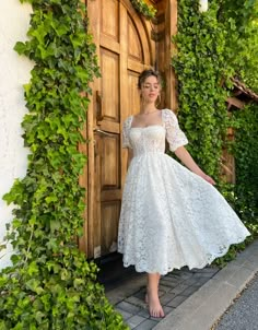 a woman standing in front of a wooden door wearing a white dress with short sleeves