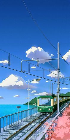 a green train traveling down tracks next to the ocean under a blue sky with clouds