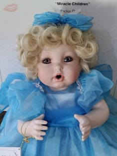 a doll with blonde hair wearing a blue dress and holding her hand out to the side