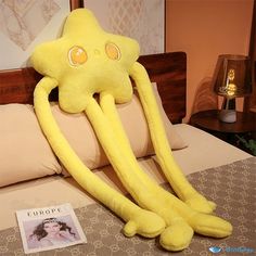 a yellow octopus stuffed animal laying on top of a bed next to a magazine and lamp