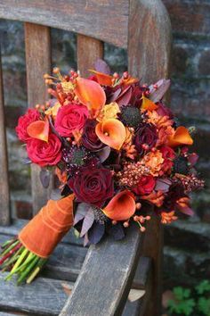 an orange and red bouquet sitting on top of a wooden chair next to a brick wall