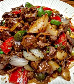 a white plate topped with meat and vegetables on top of a wooden table next to a fork