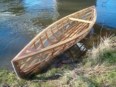 a wooden boat sitting on top of a body of water next to grass and trees