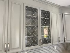 a kitchen with white cabinets and gray tile backsplashing, glass doors on the front