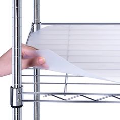 a person holding a piece of paper in front of a metal rack with white sheets on it