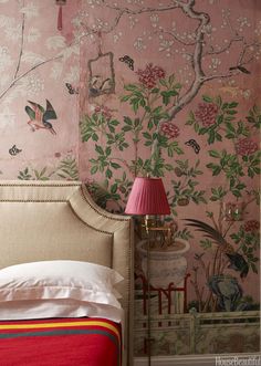 a bed sitting under a pink lamp next to a wall covered in birds and flowers