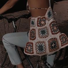 a woman is sitting on a bike wearing a crochet granny square top and jeans