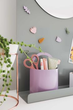 a pink container with scissors, pens and pencils in it next to a plant