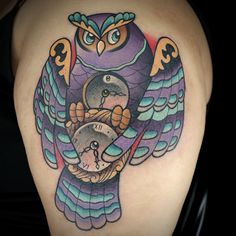 an owl tattoo on the back of a woman's shoulder, with a clock in its claws