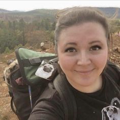 a woman taking a selfie with her dog in the back pack on top of a mountain