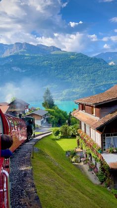 a red train traveling down tracks next to a lush green hillside covered in trees and mountains