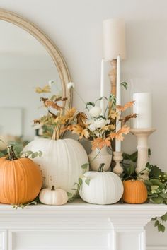 white pumpkins and greenery sit on top of a mantel in front of a mirror