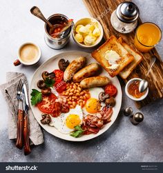 a plate with eggs, sausages, beans and toast on it next to two cups of coffee