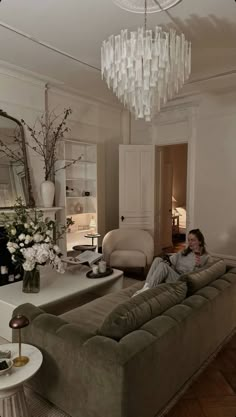 a man sitting on top of a couch in a living room under a chandelier