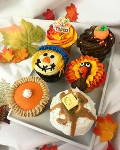 cupcakes decorated with thanksgiving decorations and fall leaves on a white platter surrounded by autumn leaves