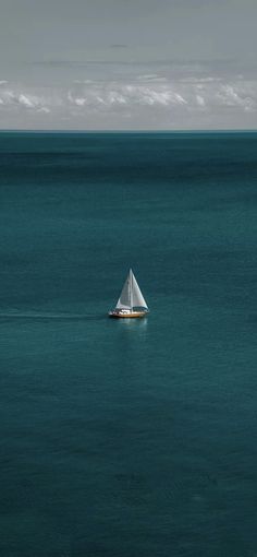 a lone sailboat in the middle of blue water