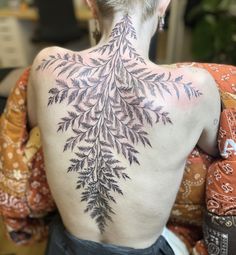 the back of a woman's body with tattoos on it, showing leaves and flowers