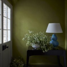 a blue vase sitting on top of a wooden table next to a lamp and window