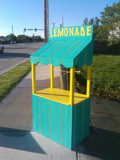 a yellow and blue lemonade kiosk sitting on the side of a road