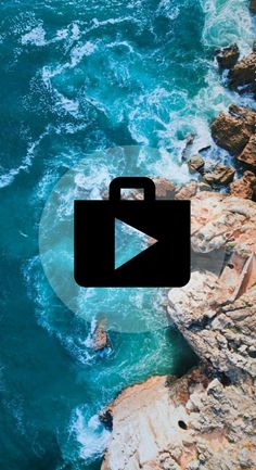 an aerial view of the ocean with rocks and blue water in the foreground, which is surrounded by rocky coastline