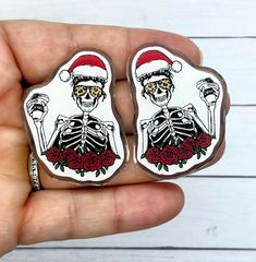 someone is holding two pin badges in their hand, one with a skeleton and roses on it