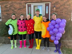 a group of people in costumes standing next to each other on the sidewalk with balloons