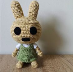 a crocheted bunny doll sitting on top of a wooden table next to a white wall