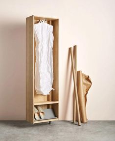 an open wooden cabinet with clothes hanging on the door and two pairs of shoes next to it