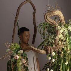 a man standing in front of some flowers and branches with his face close to the ground