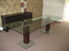 a glass table with metal legs in an empty room, next to a wallpapered wall