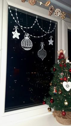 a christmas tree in front of a window with ornaments hanging from it's sides