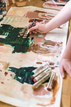 a person is painting on a piece of paper with paintbrushes and watercolors