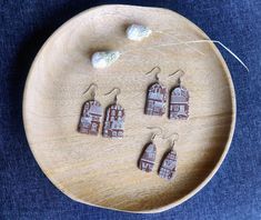 small wooden earrings with houses on them are sitting on a plate next to some thread