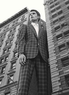 a black and white photo of a man in a suit standing next to a tall building