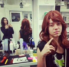 a woman with red hair in front of a mirror pointing to the side while another woman stands behind her