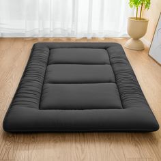 a black futon mattress sitting on top of a wooden floor next to a potted plant