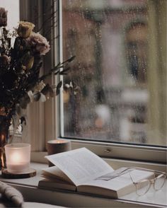 an open book sitting on top of a window sill next to a vase filled with flowers